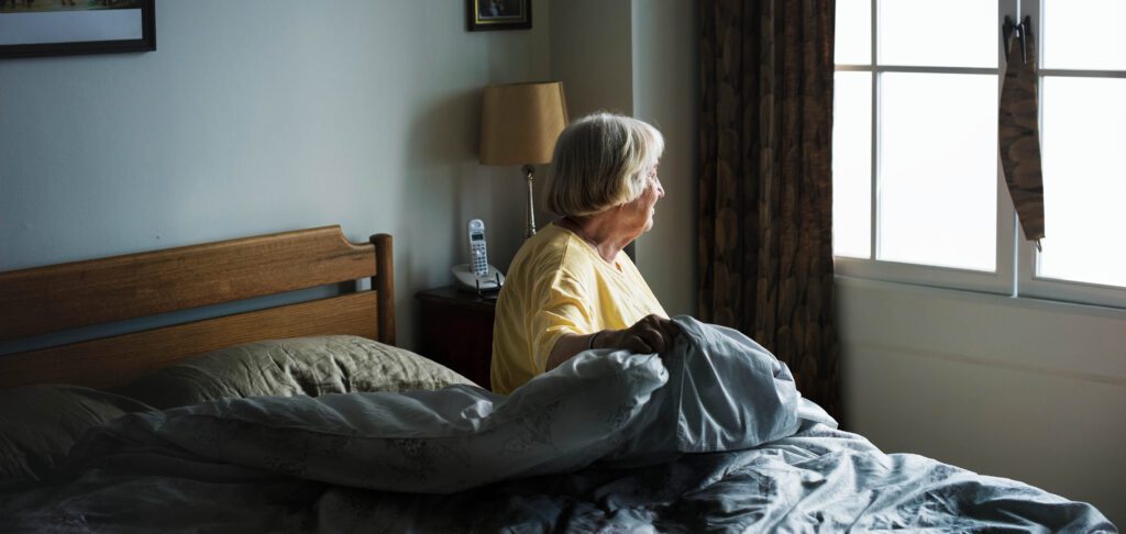 Personne âgée qui est assise sur son lit dans sa chambre