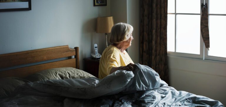 Personne âgée qui est assise sur son lit dans sa chambre