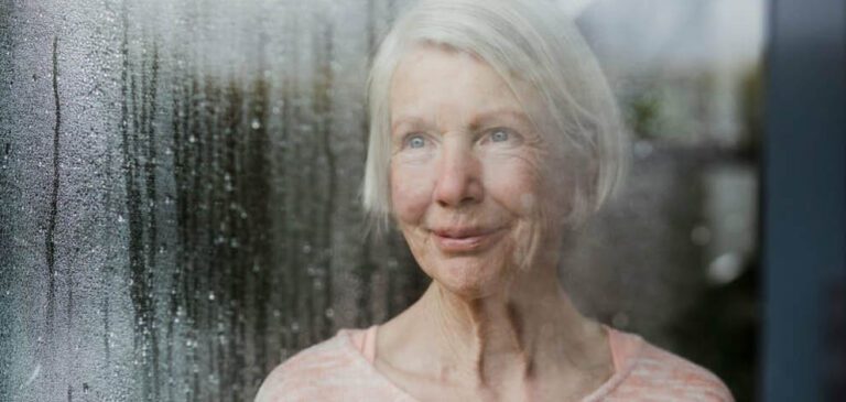 Une senior regarde la pluie par la fenêtre