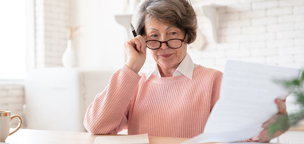 Une femme agée examinant attentivement des documents financiers, symbolisant la planification de la pension de réversion.